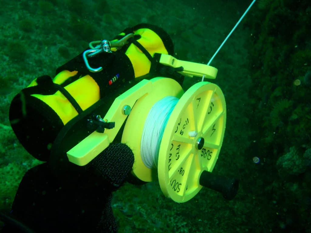 Plastic general purpose ratchet dive reel with rolled up DSMB attached with bungee loops.
