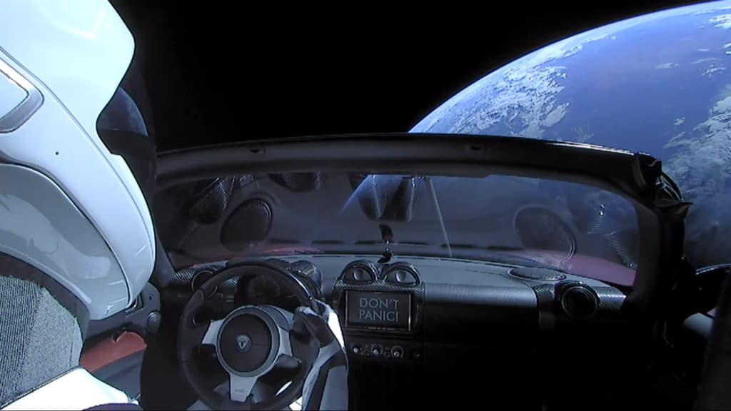 Elon Musk's Tesla Roadster , with Earth in background. "Spaceman" mannequin wearing SpaceX Spacesuit in driving seat. Hitchhiker's Guide to the Galaxy "Don't Pa