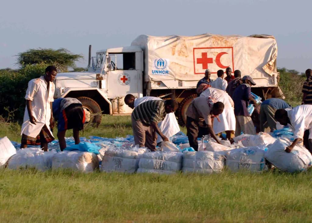 Workers from the United Nations High Commissioner for Refugees, UNHCR, and CARE gather bundles of shelters and mosquito nets that have been dropped from a U.S.