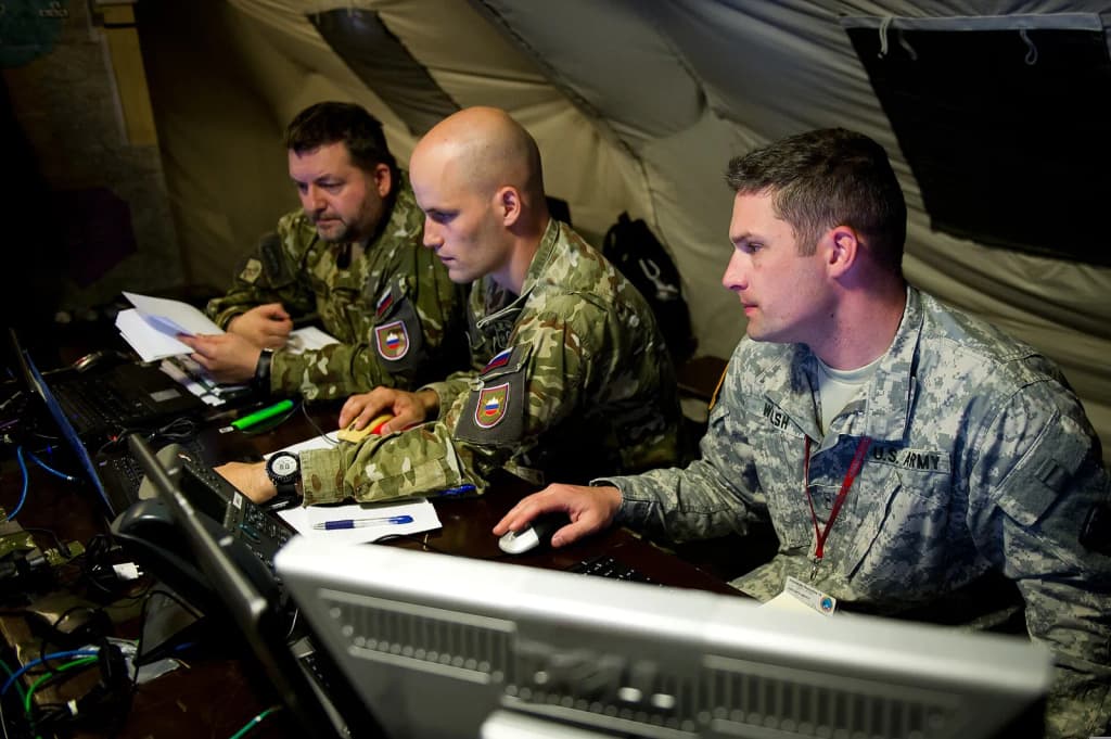 U.S. Army Chief Warrant Officer Welsh, right, with the Colorado Army National Guard, works with Slovenian soldiers during a computer-simulated exercise as part